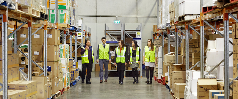 Five people in hi-vis vests walk through the corridor of a large warehouse.