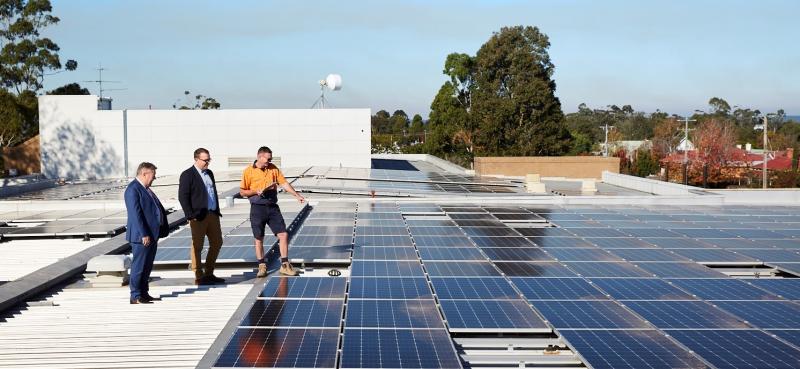 Three men stand on the roof of Sale Hospital admiring the many solar panels.